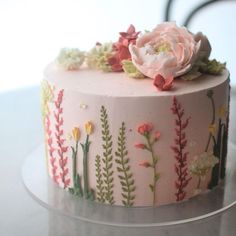 a pink cake decorated with flowers and leaves on a glass platter, sitting on a table