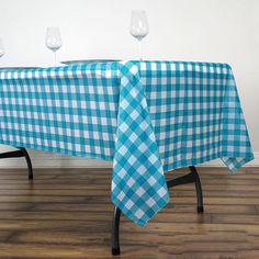 a blue and white checkered tablecloth with wine glasses on it is shown in front of a wall