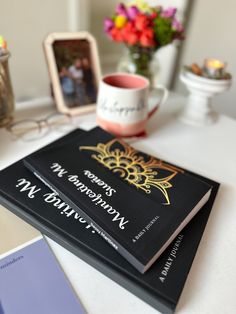 two black books sitting on top of a white table next to a vase with flowers