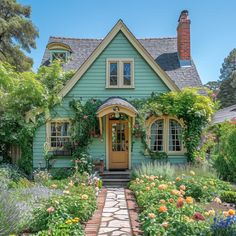 a green house with lots of flowers and plants around it's front door, surrounded by greenery