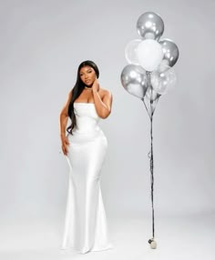 a woman in a white dress standing next to a bunch of silver and white balloons