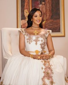 a woman sitting in a chair wearing a white dress with gold details on the skirt