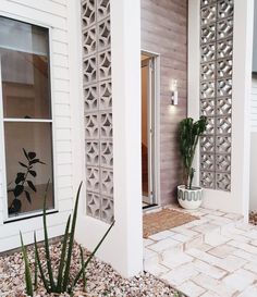 a white house with some plants in the front yard and on the side door is a potted plant