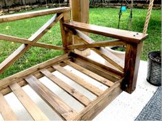 a wooden swing sitting on top of a grass covered yard next to a fence and tree