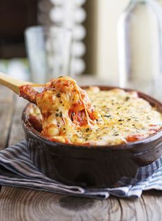 a wooden spoon is holding up a cheesy dish