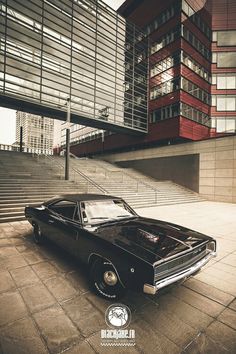 an old black car parked in front of a tall building with stairs and railings