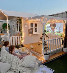 two people sitting on a couch in front of a house with christmas lights around it