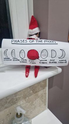 an elf is sitting on the edge of a bathroom sink holding a sign that says phases of the moon