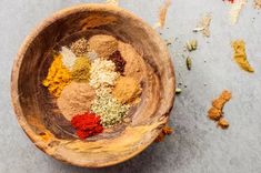 a wooden bowl filled with spices on top of a gray counter next to an orange and red pepper