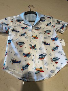 Classy crisp Airplane-Themed button-down shirt for either boys or girls.  What could be better than a nice, button-down shirt?  This version is made up of 100% white cotton printed with airplanes, clouds, helicopters, and stars  The inside yoke is made of 100% cotton blue and white striped fabric.  The shirt-tails are rounded for a more relaxed look. Available in a child's size 8 and Baby size 18-24 months.  Matching striped shorts available in size 18-24 elsewhere in this shop. Collared Shirt For School In Summer, Collared Summer Shirt For School, Short Sleeve Shirt For Playtime, Casual Buttoned Shirt For Playtime, Cotton Shirt With Button Closure For Playtime, Casual Playtime Shirt With Buttons, Summer School Shirt With Buttons, Summer Playtime Shirt With Button Closure, Summer Playtime Shirt