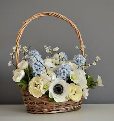 a basket filled with white and blue flowers on top of a table next to a gray wall