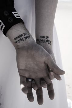 two people with tattoos on their arms holding hands and one has the words in black ink