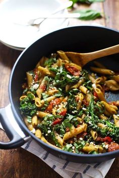 a pan filled with pasta and spinach on top of a wooden table