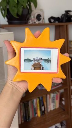 a person holding up a yellow sun shaped photo frame with an image of two people on it