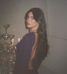 a woman standing next to a table with candles on it and wearing a purple dress