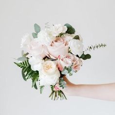 a woman holding a bouquet of white and pink flowers with greenery in her hand