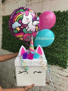 a box filled with balloons and a unicorn face on it's side, sitting next to a wall