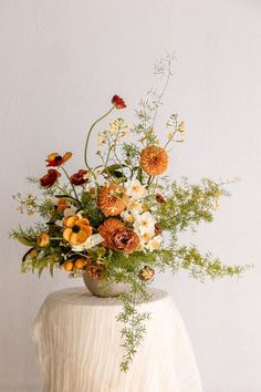 a vase filled with lots of flowers sitting on top of a white table covered in greenery