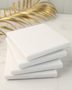 four white coasters stacked on top of each other with gold leaves in the background