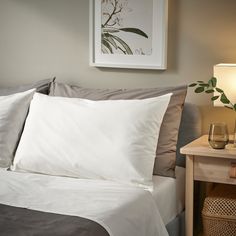 a bed with white sheets and pillows next to a lamp on a nightstand in a bedroom