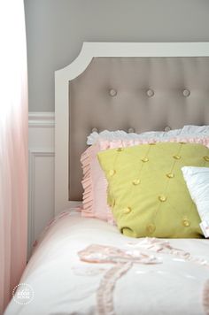 a bed with pink and yellow pillows on top of it's headboard next to a window