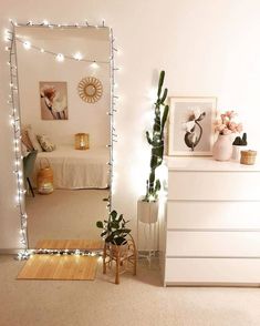 a bedroom with white furniture and string lights on the wall, along with a large mirror