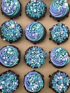 twelve decorated cookies in a box with blue frosting and white sprinkles