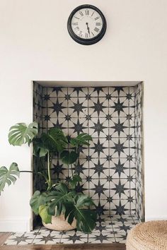 a clock mounted on the wall above a potted plant in front of a black and white tiled niche