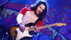 a man with long hair playing an electric guitar in front of a microphone on stage