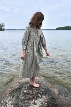 a woman standing on top of a rock in the water next to a body of water