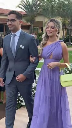 a woman in a purple dress and a man in a gray suit are walking together