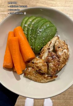 a white plate topped with chicken, carrots and cucumber next to a green leaf