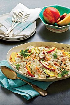 a bowl filled with pasta and fruit on top of a table next to silverware