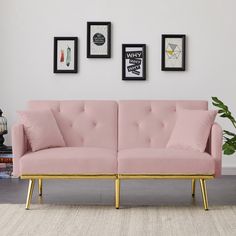 a pink couch with gold legs in front of three framed pictures and a potted plant