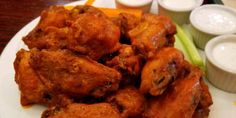 a white plate topped with chicken wings and celery next to two small bowls