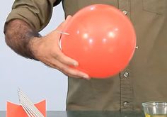 a man holding an orange balloon in front of a glass and knife on a table