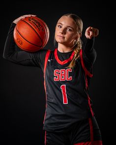 a female basketball player holding a ball in her right hand and posing for the camera