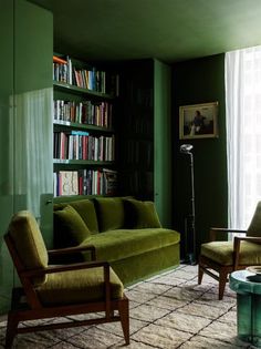 a living room filled with green furniture and bookshelves next to a large window