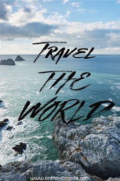 the words travel the world written in black ink on a rocky cliff overlooking the ocean