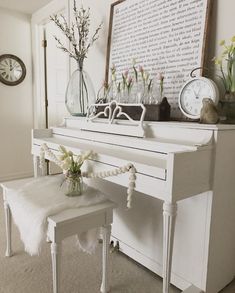 a white piano sitting in front of a wall with flowers on it and a clock