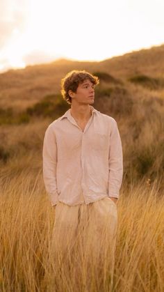 a young man standing in tall grass looking off into the distance with his hands in his pockets