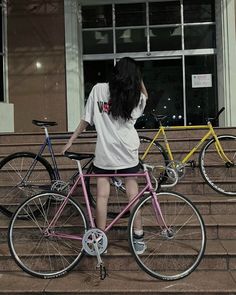 a woman sitting on the steps next to her bike and looking at another person's bicycle