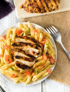 a white plate topped with pasta and chicken next to a cutting board filled with meat