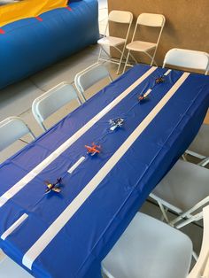 there are many toy airplanes on the blue table cloth at this birthday party with white chairs