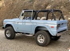 a light blue jeep parked on the side of a dirt road next to a hill