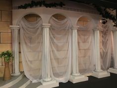 some white pillars with curtains on them and a potted plant in the corner next to them