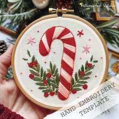 a hand embroidered candy cane with holly wreaths and stars on it in front of a christmas tree