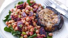 a white plate topped with meat and beans next to a salad on top of a table