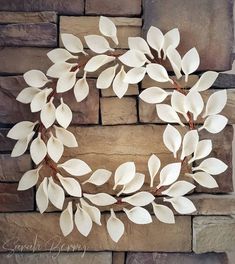 a wreath made out of white leaves on top of a brick wall next to a stone wall