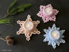 three crocheted snowflakes with lit candles in them